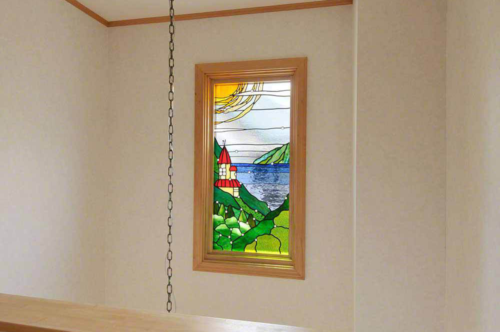 山の中腹にある赤い屋根のお城、湖の向こう側にある島と大きな太陽が描かれたステンドグラスの風景画。