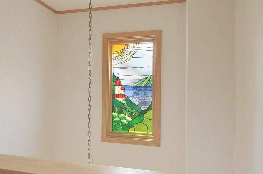 山の中腹にある赤い屋根のお城、湖の向こう側にある島と大きな太陽が描かれたステンドグラスの風景画。