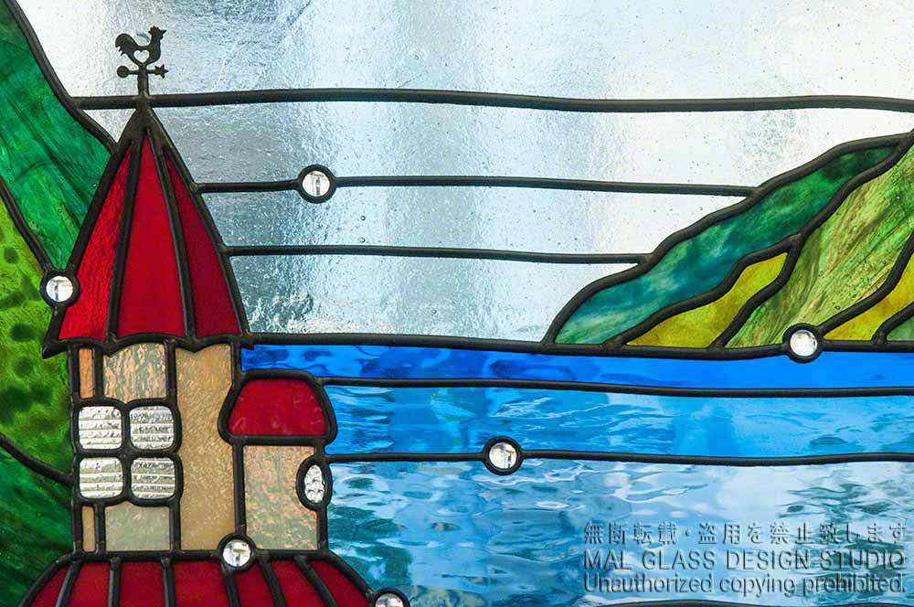 風見鶏がかわいい赤い屋根のお城と湖のクローズアップ写真。具象的なステンドグラスの施工例。