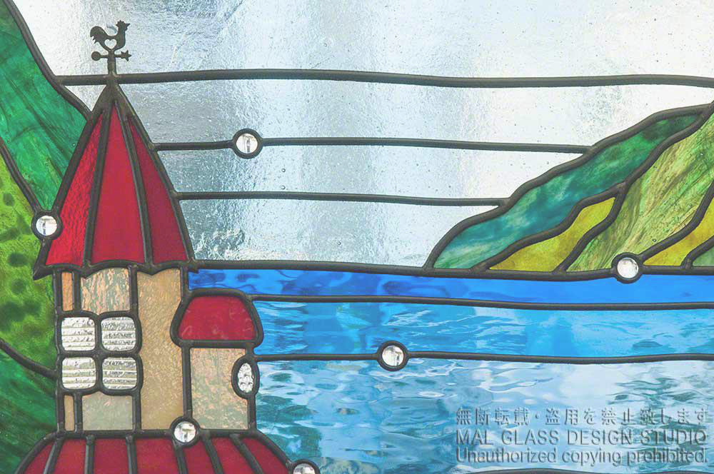 風見鶏がかわいい赤い屋根のお城と湖のクローズアップ写真。具象的なステンドグラスの施工例。