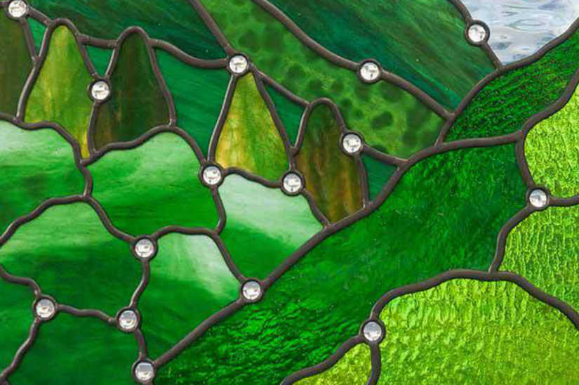 柔らかい光を透す緑色のスティップルガラスとジュエルのクローズアップ写真。具象的なステンドグラスの施工例。