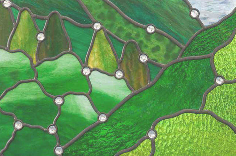 柔らかい光を透す緑色のスティップルガラスとジュエルのクローズアップ写真。具象的なステンドグラスの施工例。